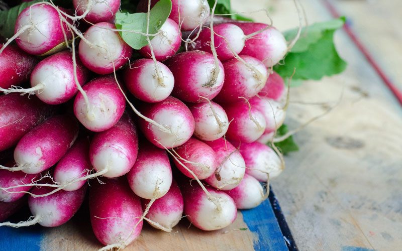 Radishes rest in a bunch on a table.