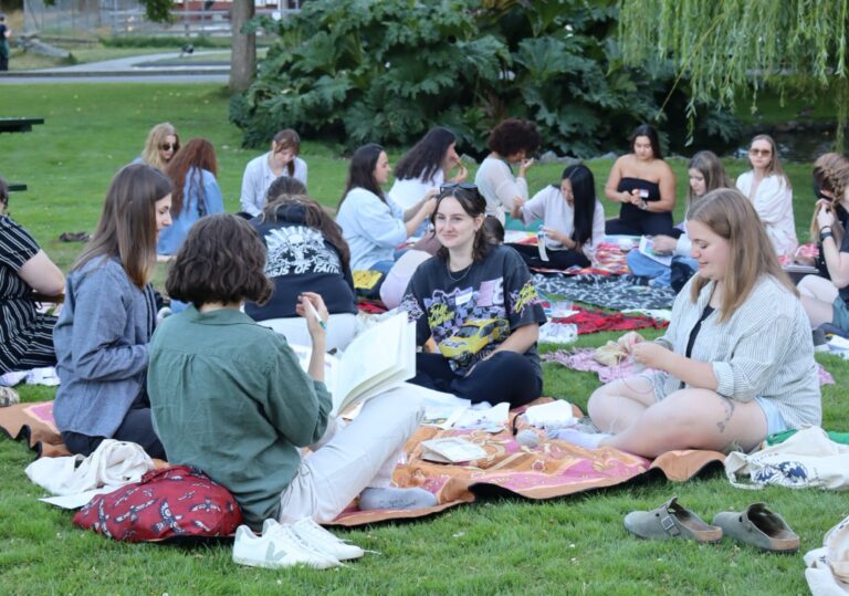 Several people sitting in multiple circles on picnic blankets in a public park.